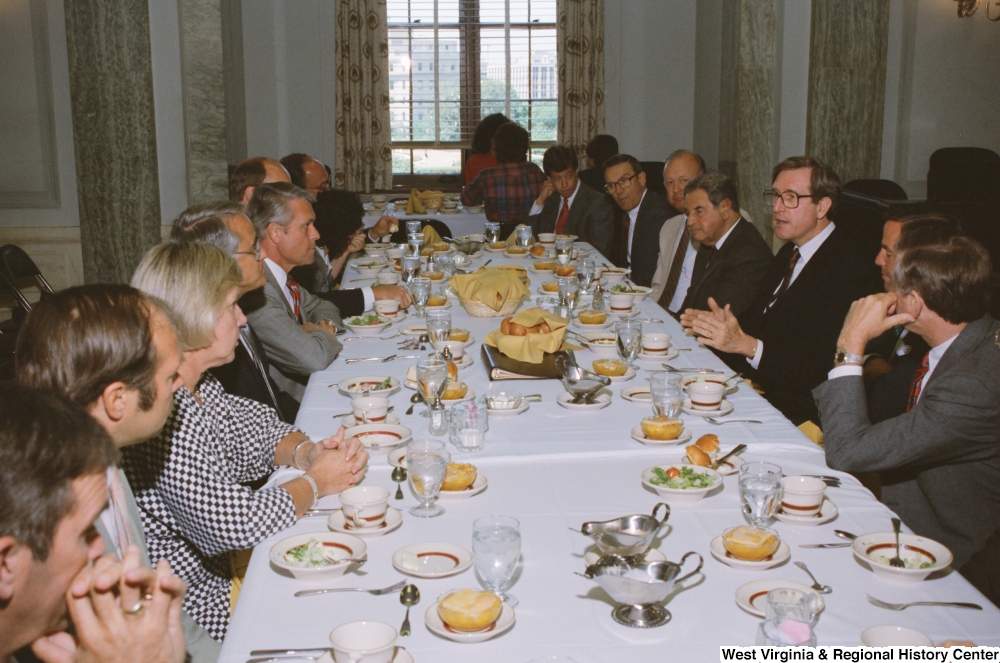 ["Senator John D. (Jay) Rockefeller sits at a banquet table with numerous unidentified individuals during an AEP reception."]%