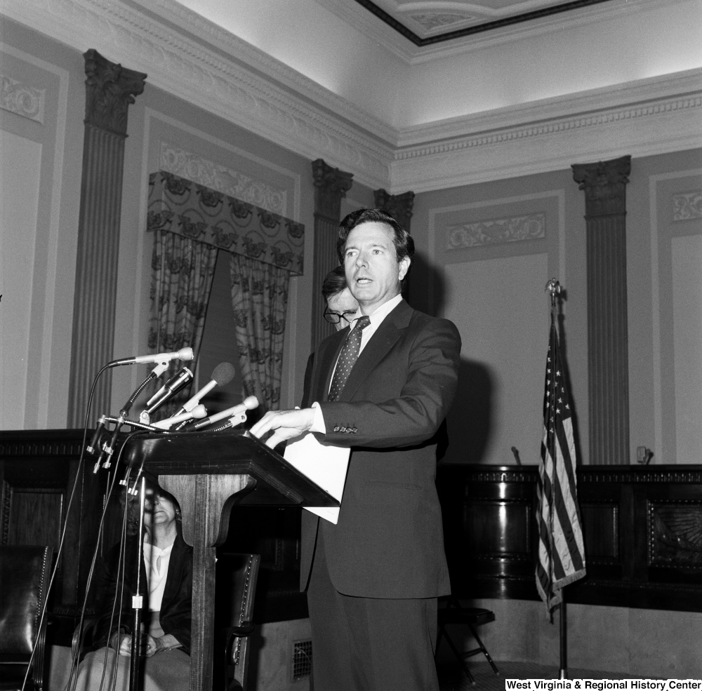 ["Senator John Heinz speaks from behind a podium. Senator John D. (Jay) Rockefeller stands behind him and looks at the floor."]%