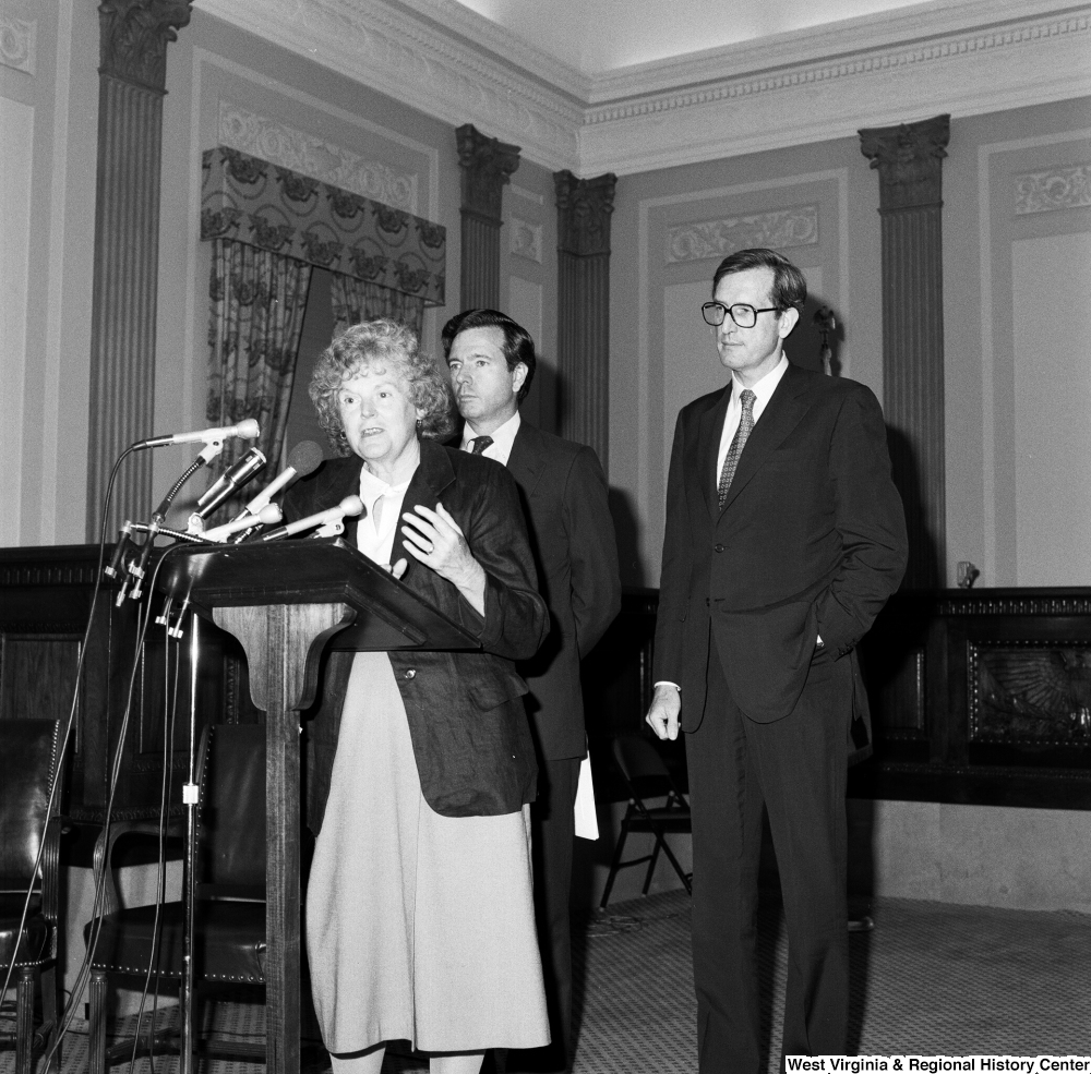 ["An unidentified woman speaks about the Dislocated Workers Improvement Act of 1987 as Senator John D. (Jay) Rockefeller and Senator John Heinz stand behind her."]%