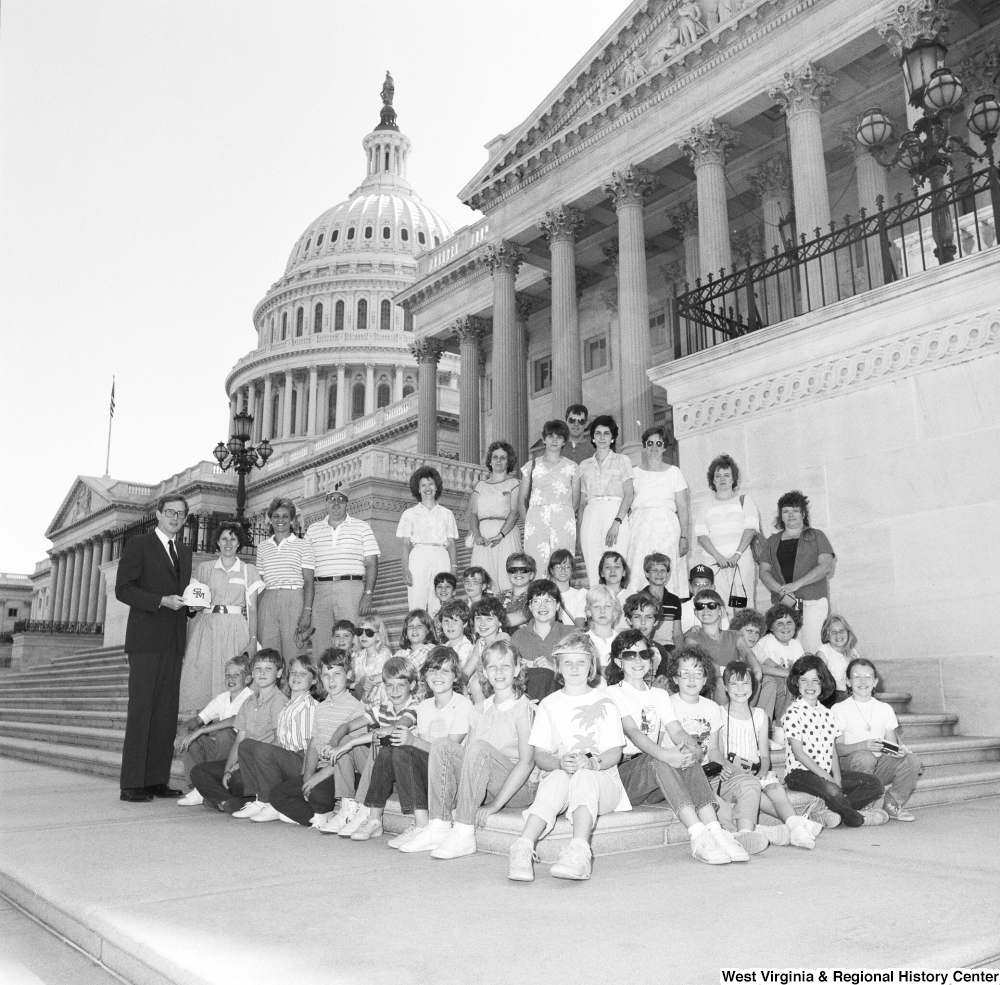 ["Senator john D. (Jay) Rockefeller stands next to a seated group of young students on the steps of the US Capitol."]%