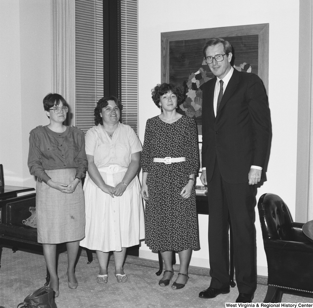 ["Senator John D. (Jay) Rockefeller stands next to three unidentified women in his office."]%
