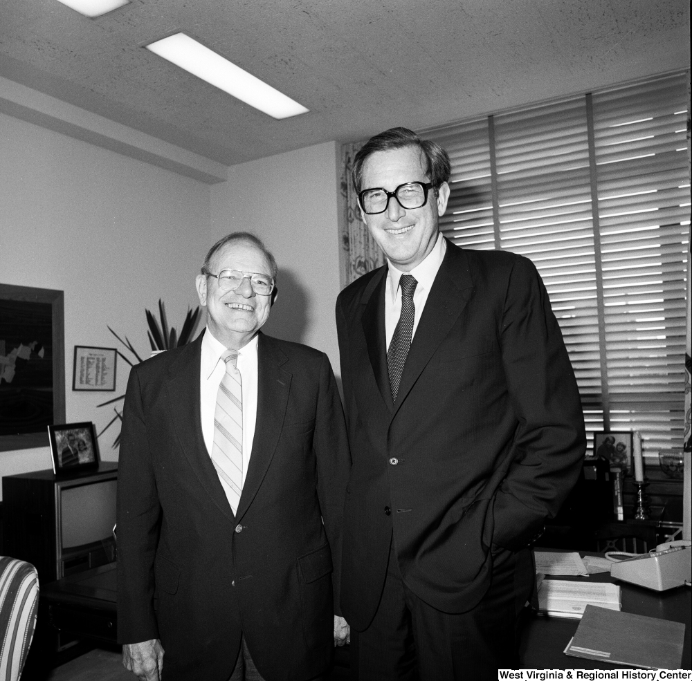 ["Senator John D. (Jay) Rockefeller stands in front of the desk in his office and poses for a photograph with an unidentified man."]%