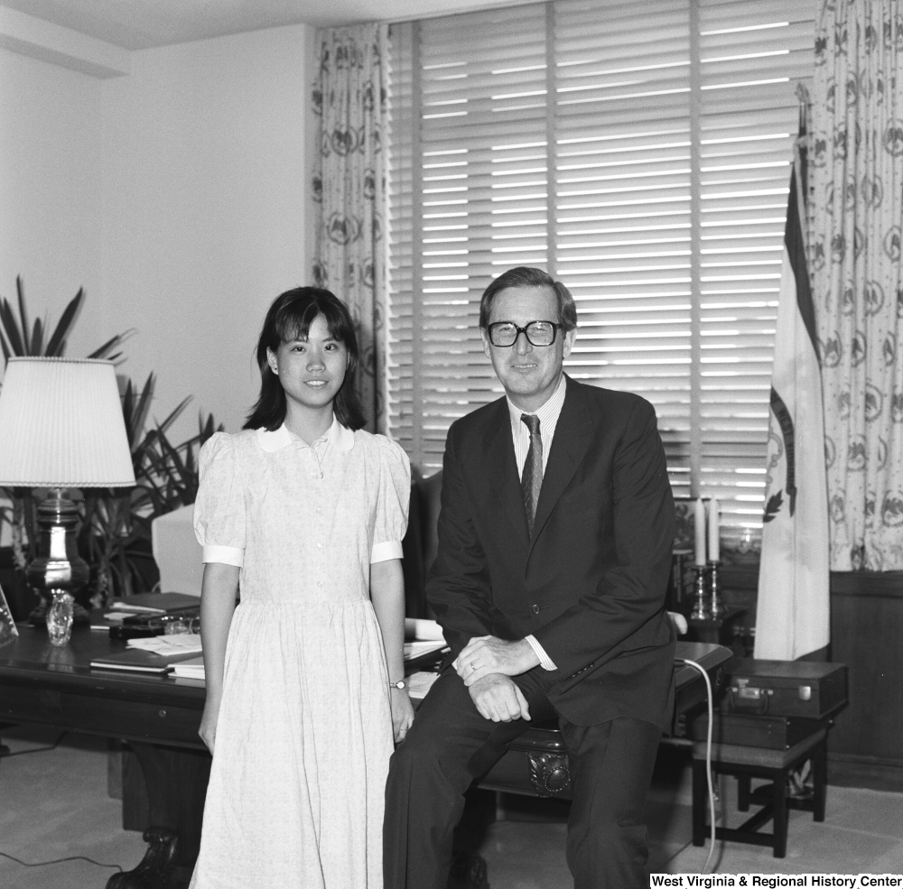 ["Senator John D. (Jay) Rockefeller sits on the corner of the desk in his office and poses for a photograph with an unidentified individual."]%