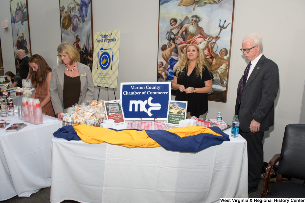 ["Two people stand at the Marion County Chamber of Commerce table at the 150th birthday celebration for West Virginia."]%