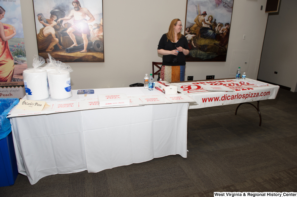 ["A woman stands at a table for DiCarlo's Pizza at the 150th birthday celebration for West Virginia."]%