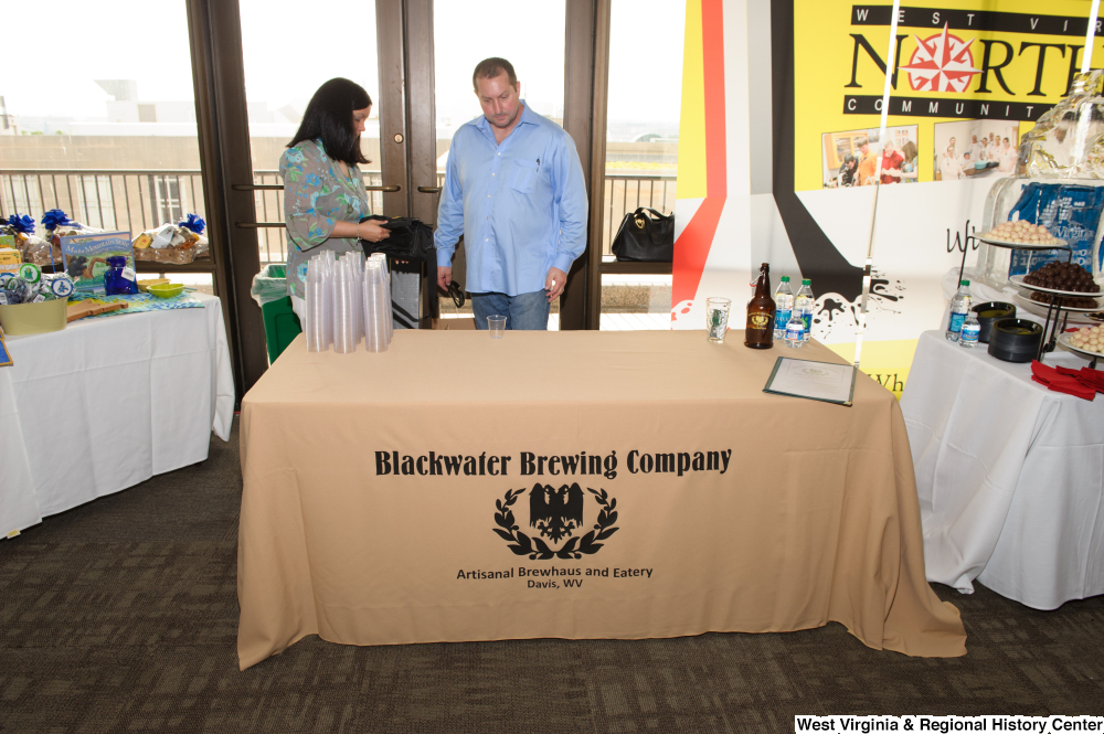 ["A man stands behind the Blackwater Brewing Company table at the 150th birthday celebration for West Virginia."]%