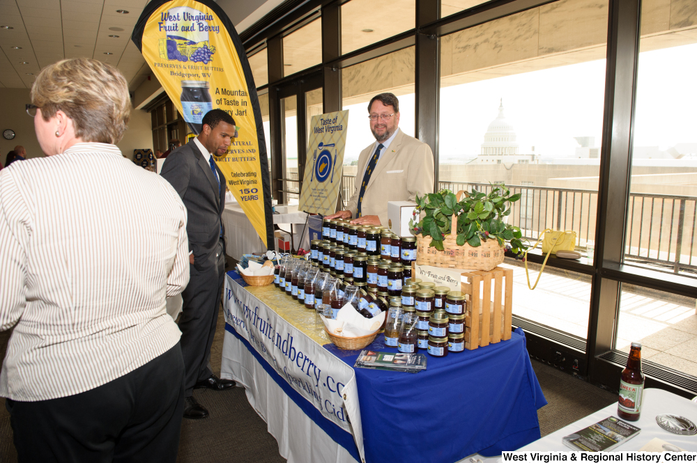 ["A man stands and looks at the West Virginia Fruit and Berry company's table during the 150th birthday celebration for the state."]%