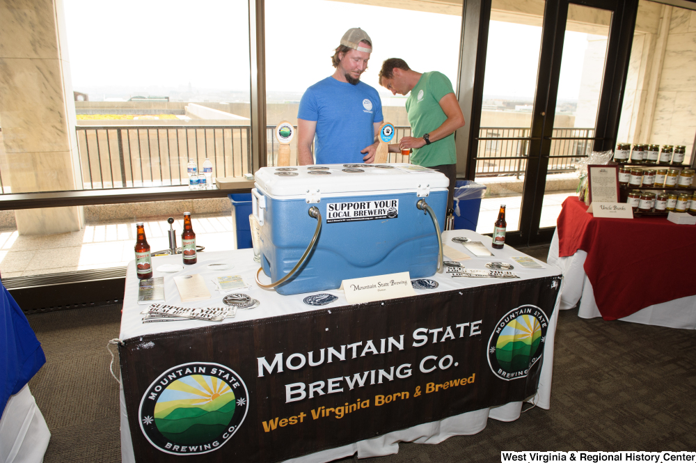 ["Two men stand behind the Mountain State Brewing Company table at the 150th birthday celebration for West Virginia."]%