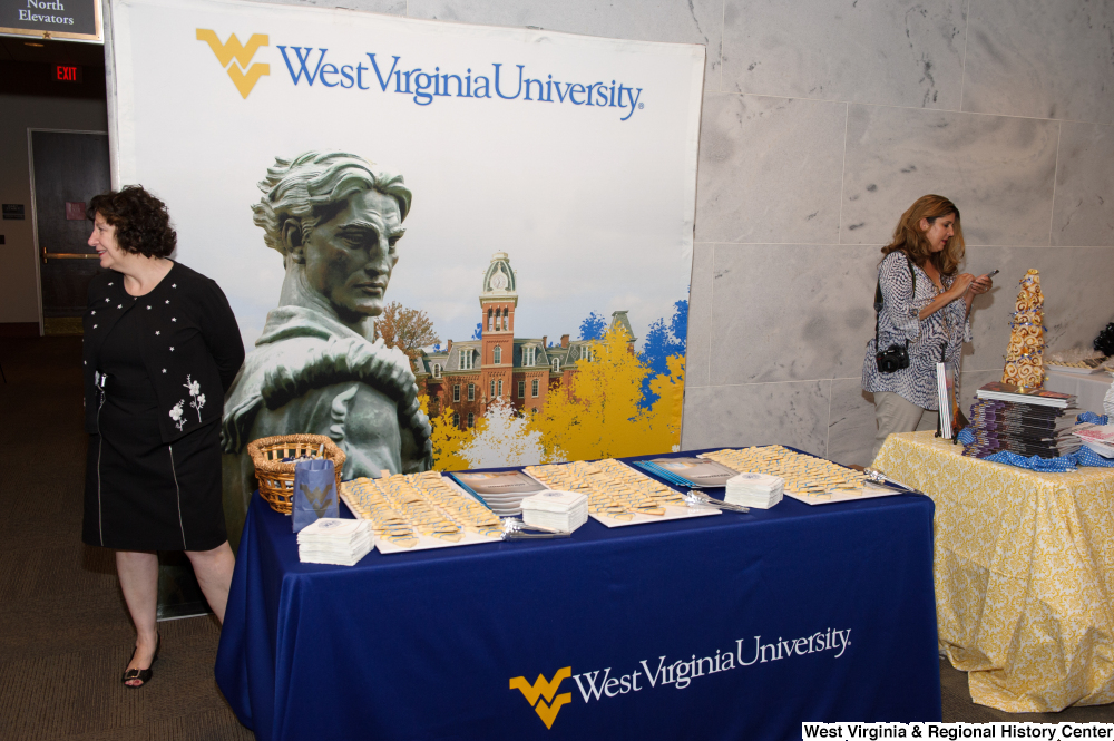 ["A woman stands behind the West Virginia University table at the state's 150th birthday celebration."]%