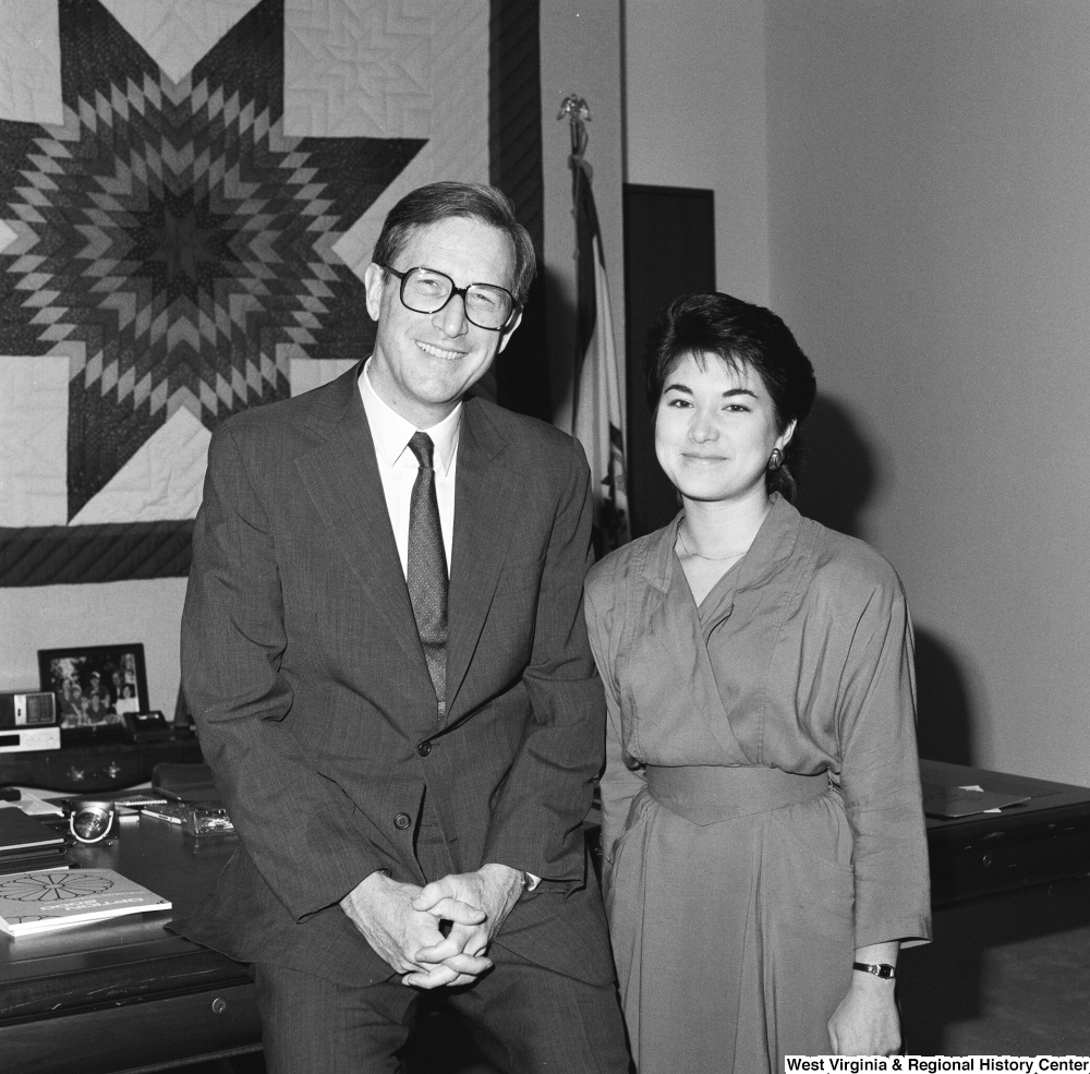 ["Senator John D. (Jay) Rockefeller sits on the corner of the desk in his office  next to an unidentified young woman."]%