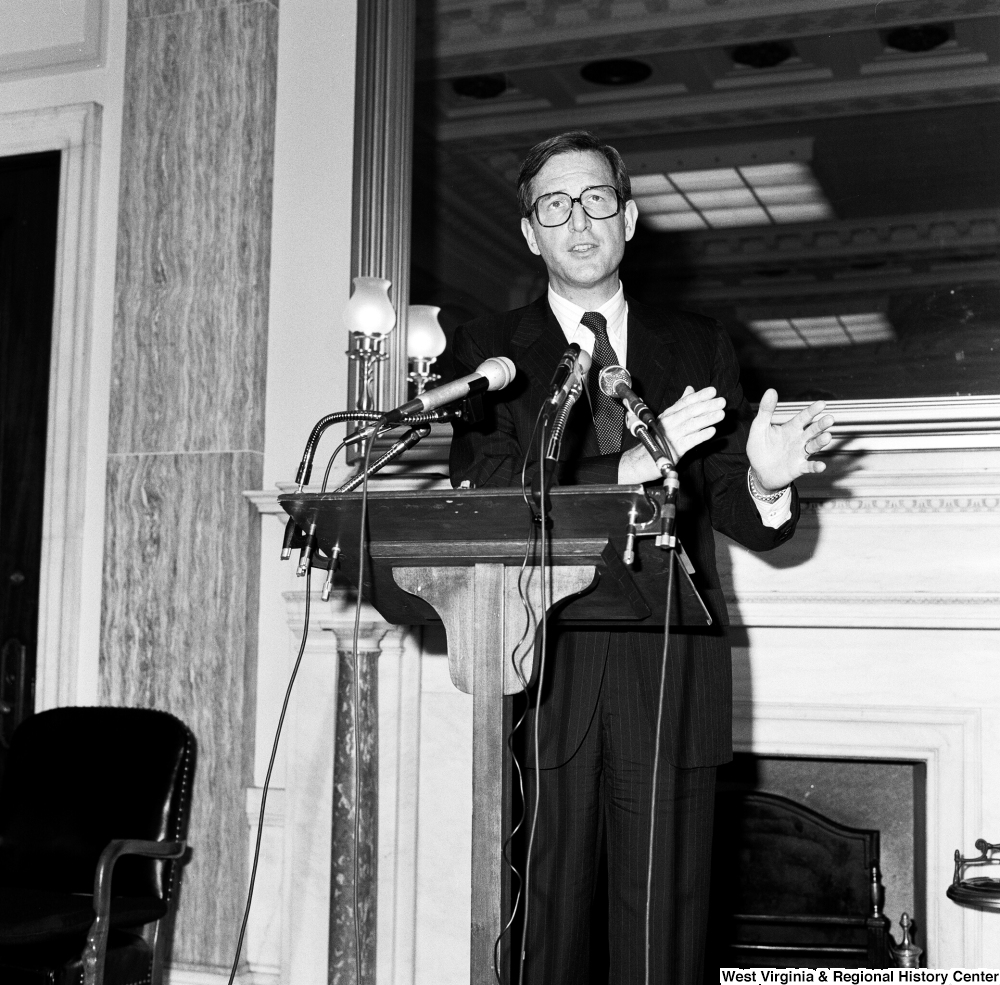 ["Senator John D. (Jay) Rockefeller speaks behind a podium at a press event in one of the Senate buildings."]%