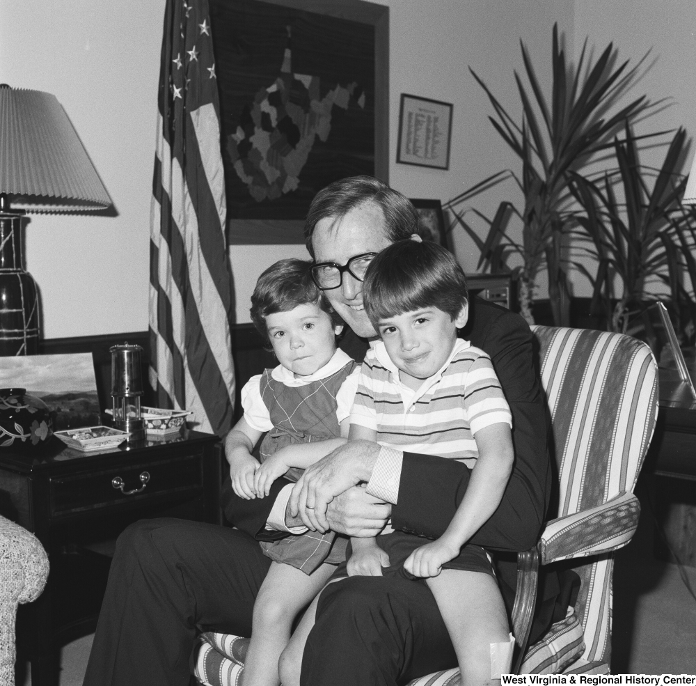 ["Senator John D. (Jay) Rockefeller holds two unidentified children on his lap while he sits in his office."]%