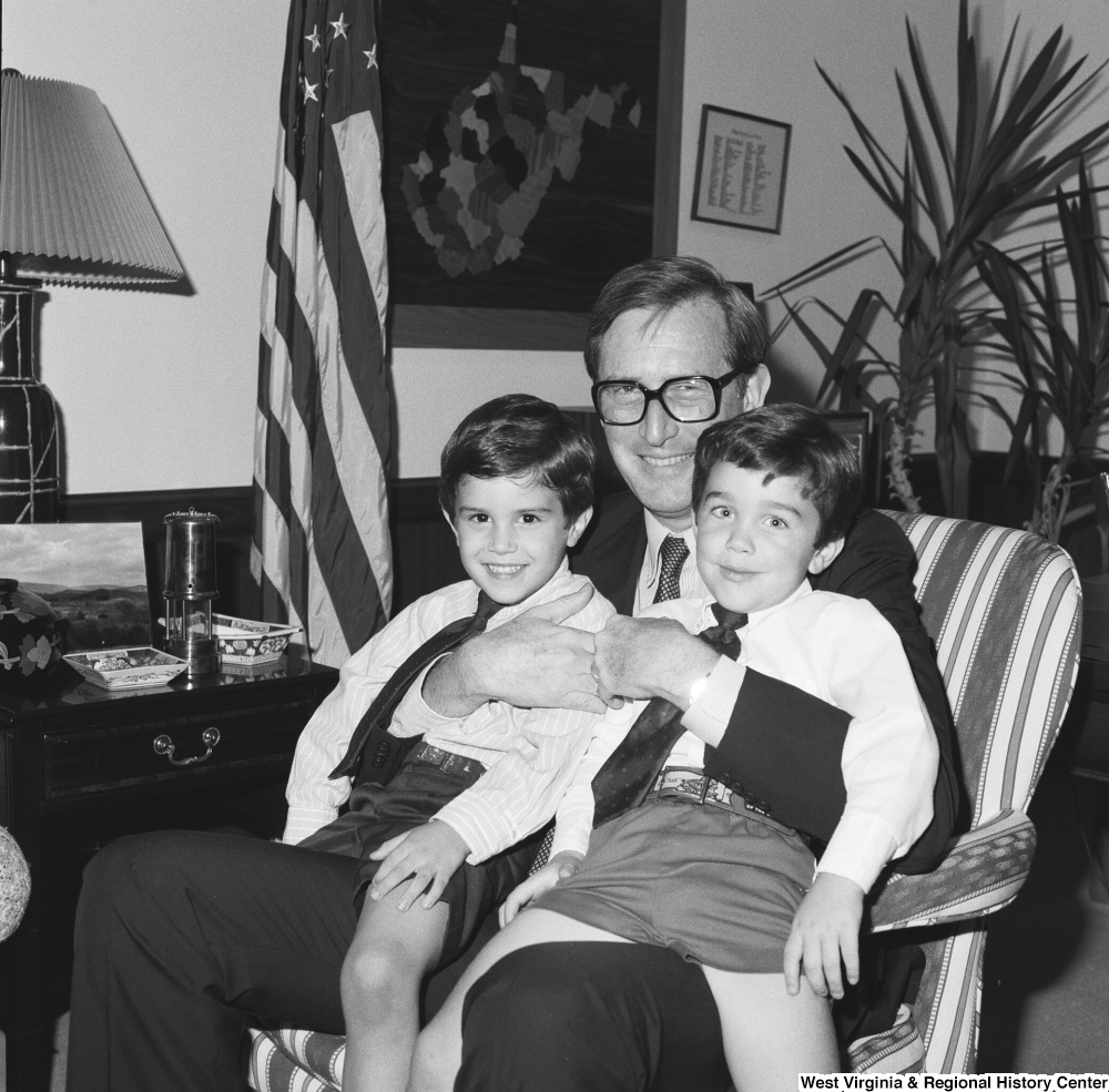 ["Senator John D. (Jay) Rockefeller holds two unidentified young boys on his lap while he sits in his office."]%