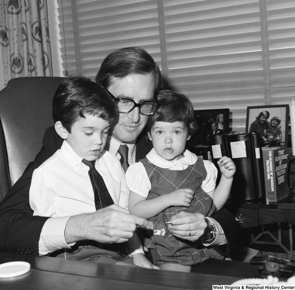 ["Senator John D. (Jay) Rockefeller holds two small children on his lap as he sits behind his desk."]%