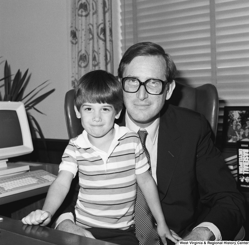 ["Senator John D. (Jay) Rockefeller holds an unidentified small child on his lap as he sits behind the desk in his office."]%