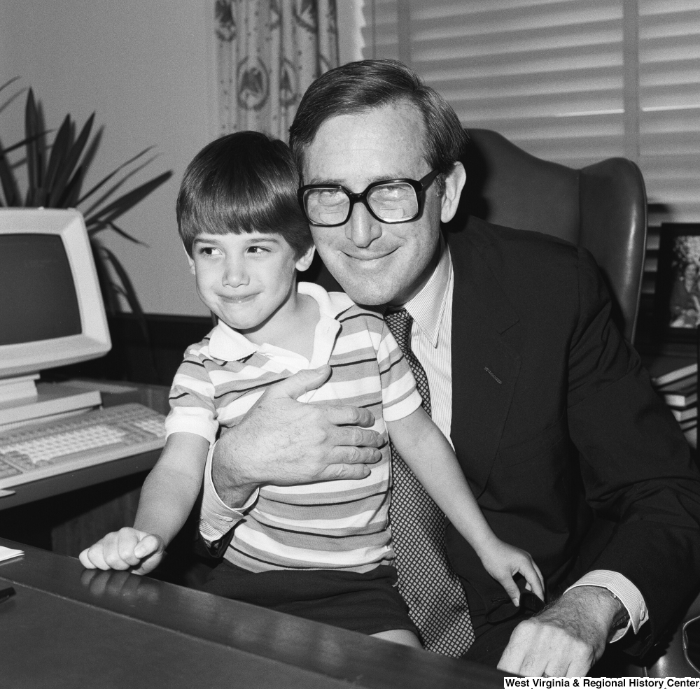 ["A small unidentified child looks away as Senator John D. (Jay) Rockefeller holds him for a photograph in his office."]%