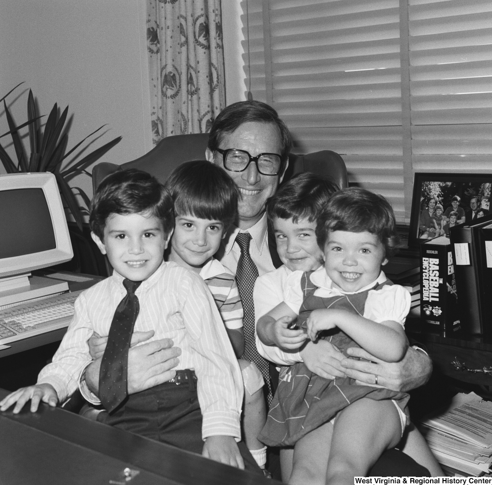 ["Senator John D. (Jay) Rockefeller holds a group of four unidentified children on his lap as he sits behind the desk in his Washington office."]%