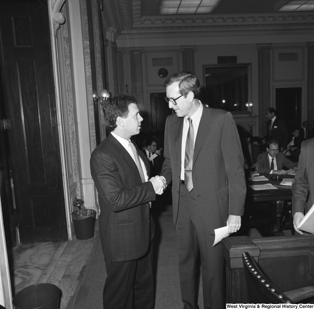 ["Senator John D. (Jay) Rockefeller shakes hands with an unidentified man in a Senate hearing room."]%