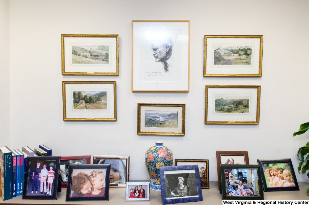 ["Many photographs and paintings hang on a wall and sit on a table in Senator John D. (Jay) Rockefeller's office."]%