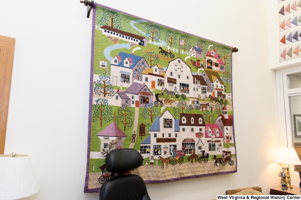 ["A quilt depicting a small town hangs on a wall in Senator John D. (Jay) Rockefeller's office."]%