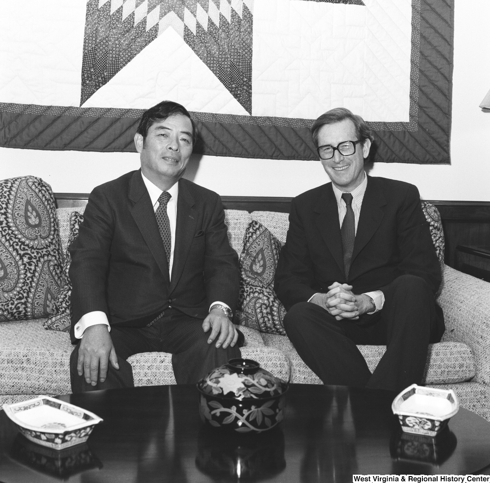 ["Senator John D. (Jay) Rockefeller sits on the couch in his office with an unidentified individual."]%