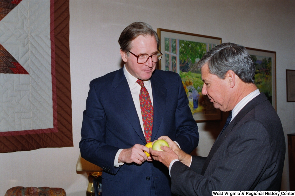 ["As Senator John D. (Jay) Rockefeller watches, Florida Senator Bob Graham inspects a West Virginia apple."]%