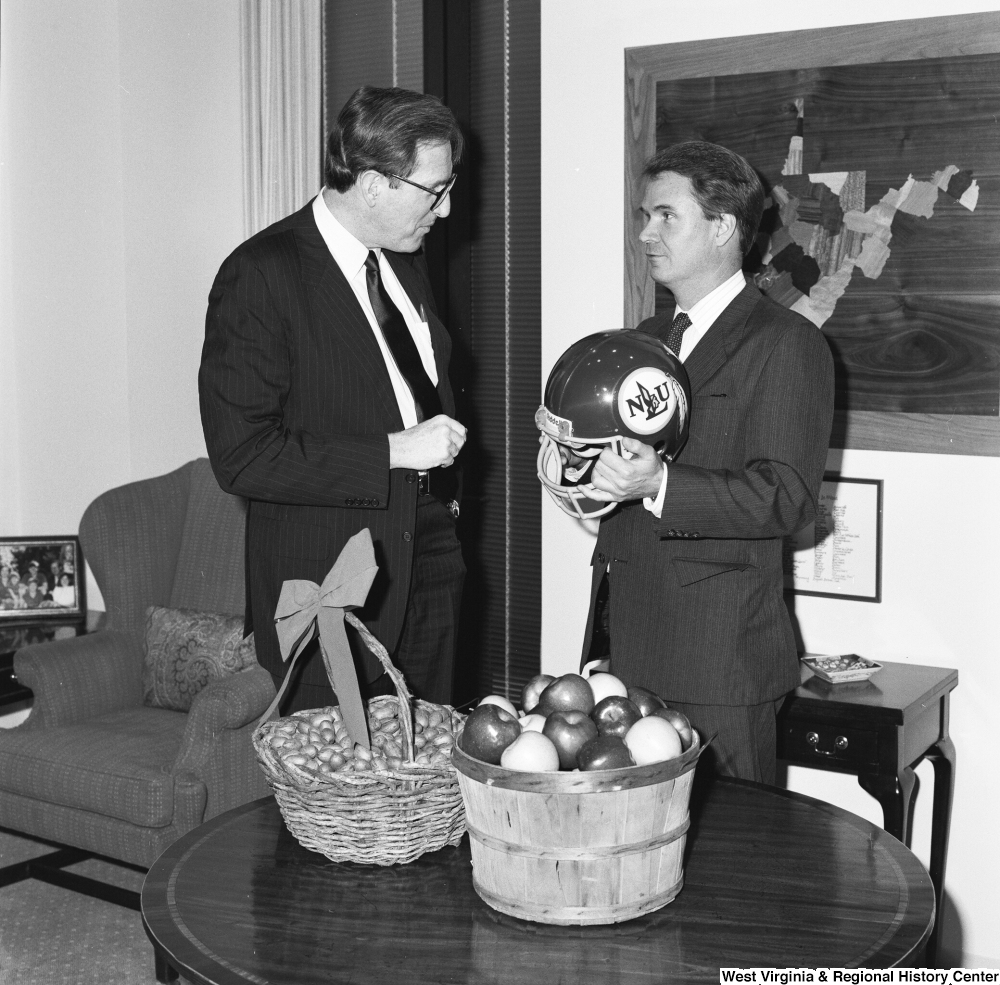 ["Senator John D. (Jay) Rockefeller stands next to Senator Breaux who is holding a football helmet. The two had a friendly bet against who would win the upcoming Marshall/NLU football game."]%