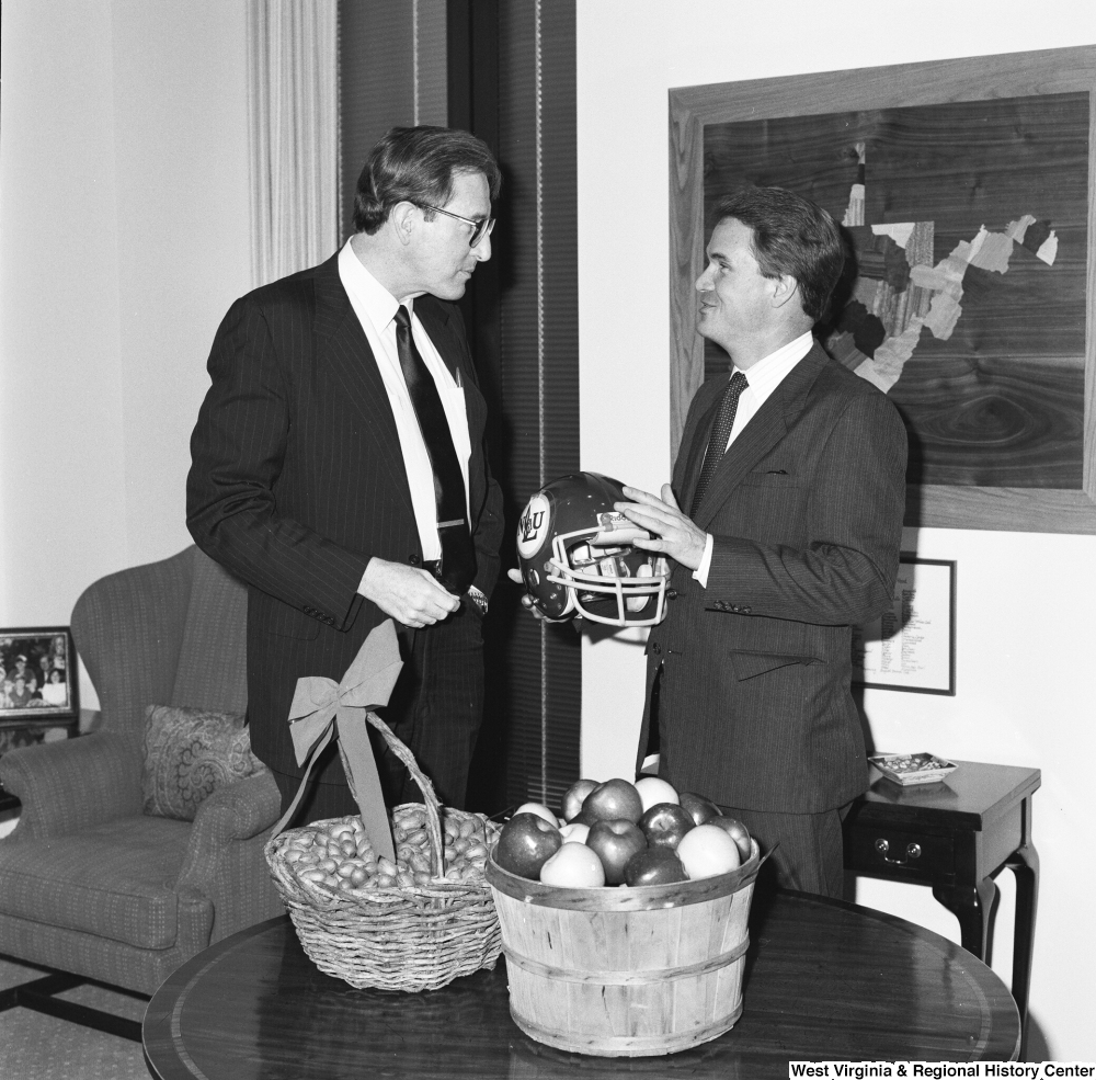 ["Senator John D. (Jay) Rockefeller speaks to Senator John Breaux who holds a football helmet."]%